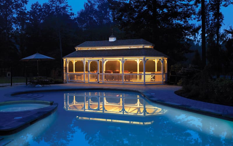 A pool with a gazebo and lights on the side.