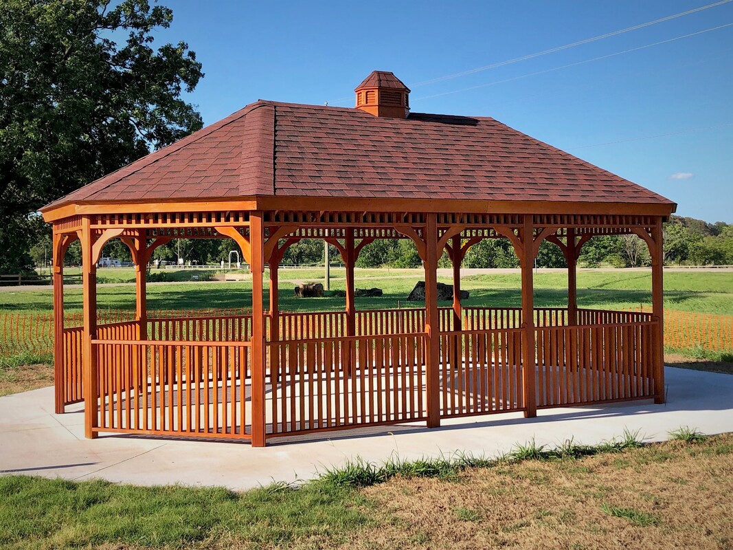 A wooden gazebo with a brick roof and fence.
