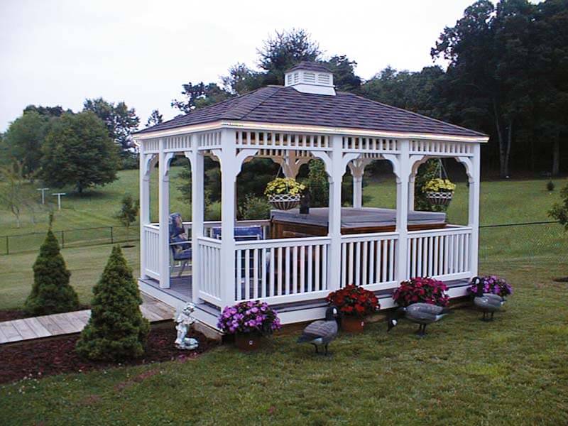 A gazebo with benches and flowers in the grass.