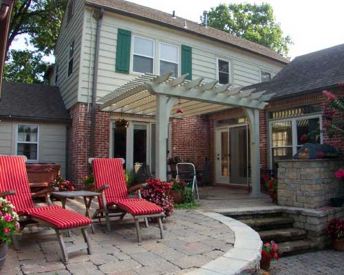A patio with chairs and a pergola in the back yard.