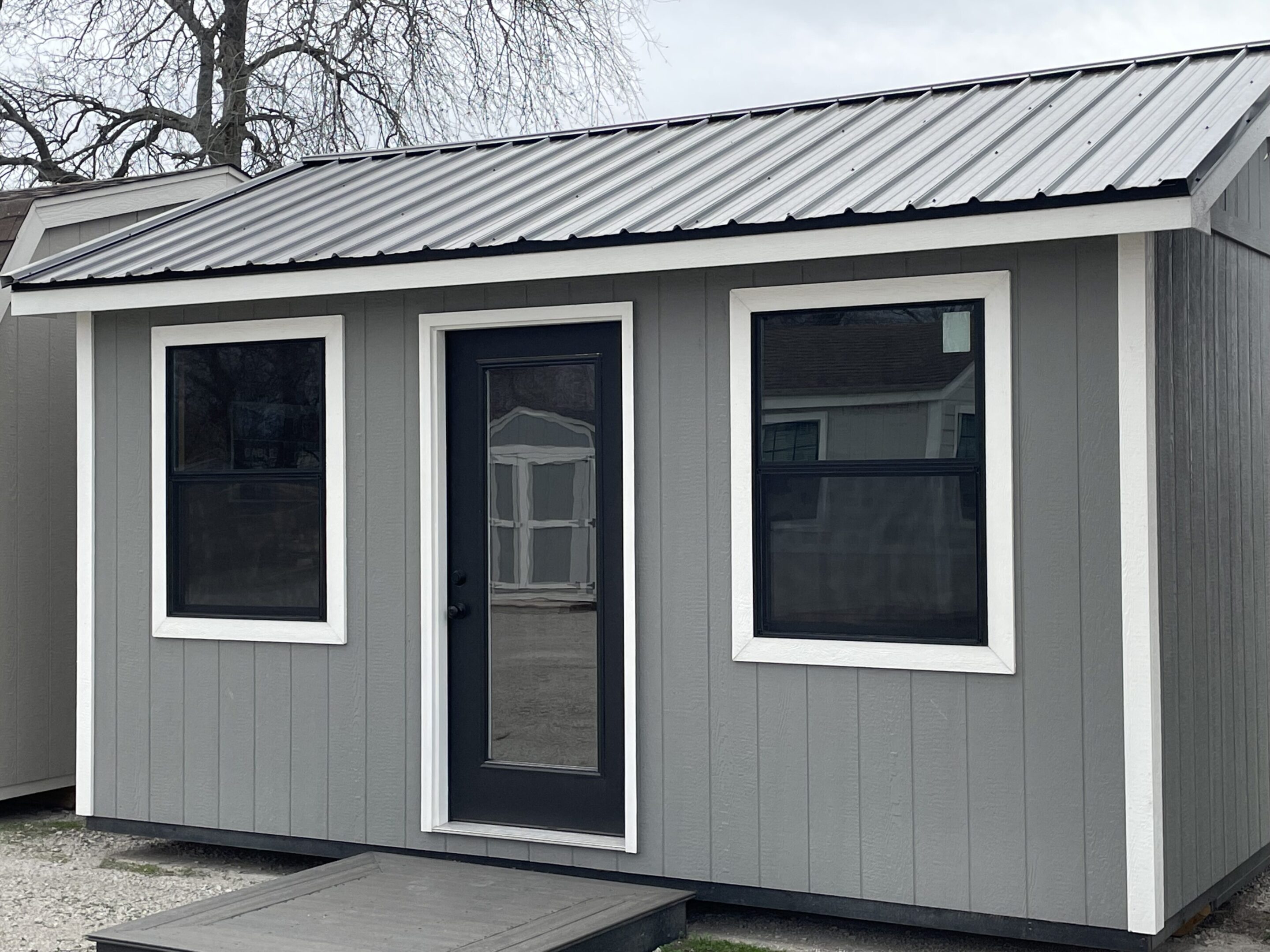 A gray shed with white trim and windows.