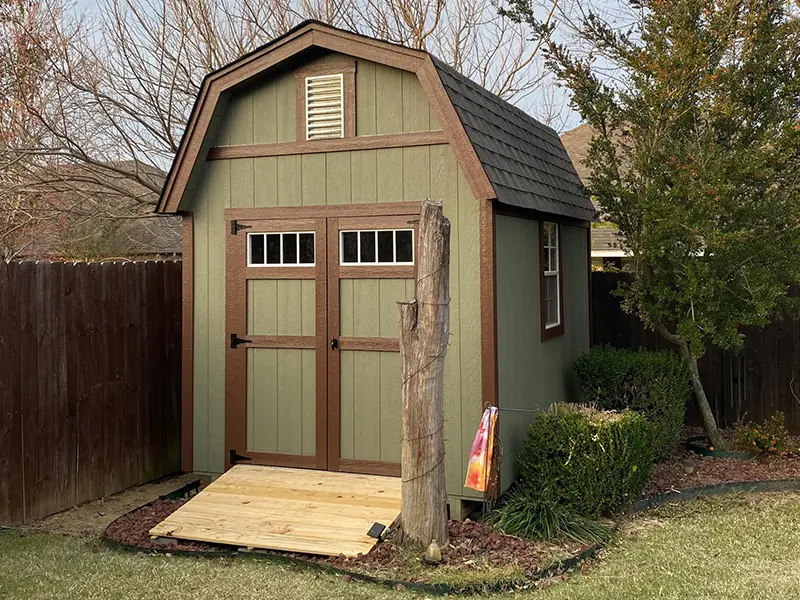 A green shed with brown trim and wood steps.